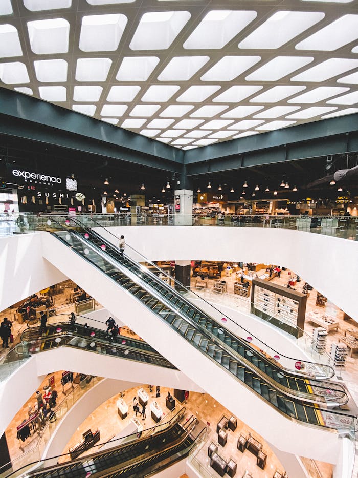 A bustling modern shopping mall with multiple escalators and retail shops in Toluca de Lerdo, Mexico.