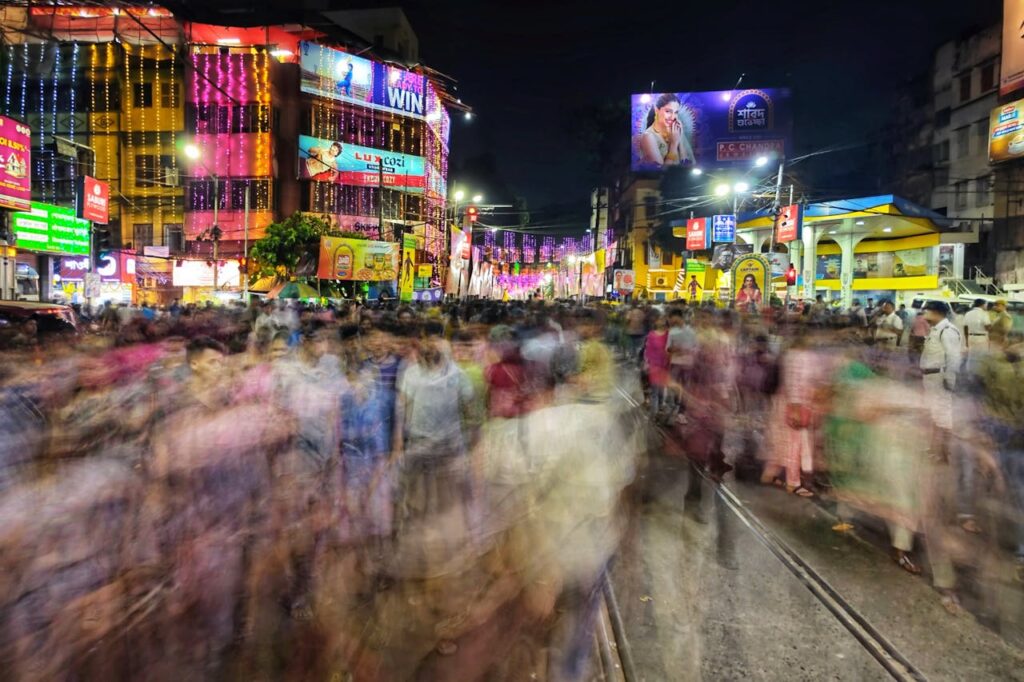 A bustling street scene in Kolkata at night, showcasing lively festival lights and blurred crowds.